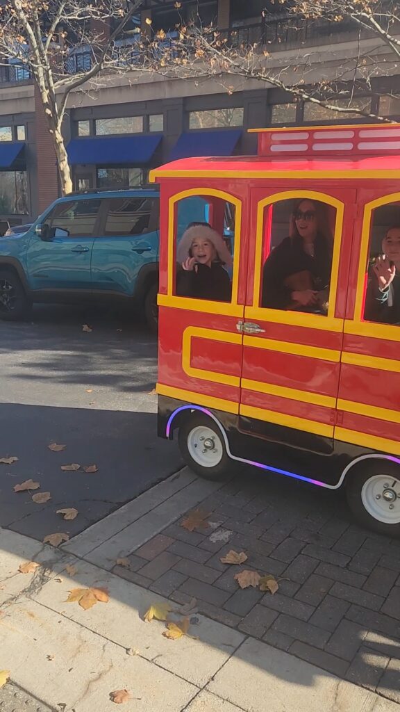 Young girl waving from the window of the All Aboard KC trackless train