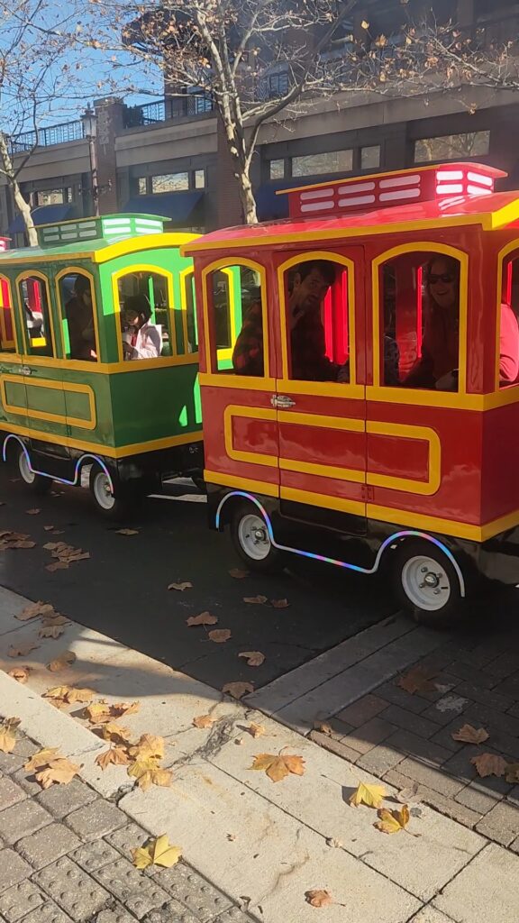 Riders waving from the green and red cars of the All Aboard KC trackless train